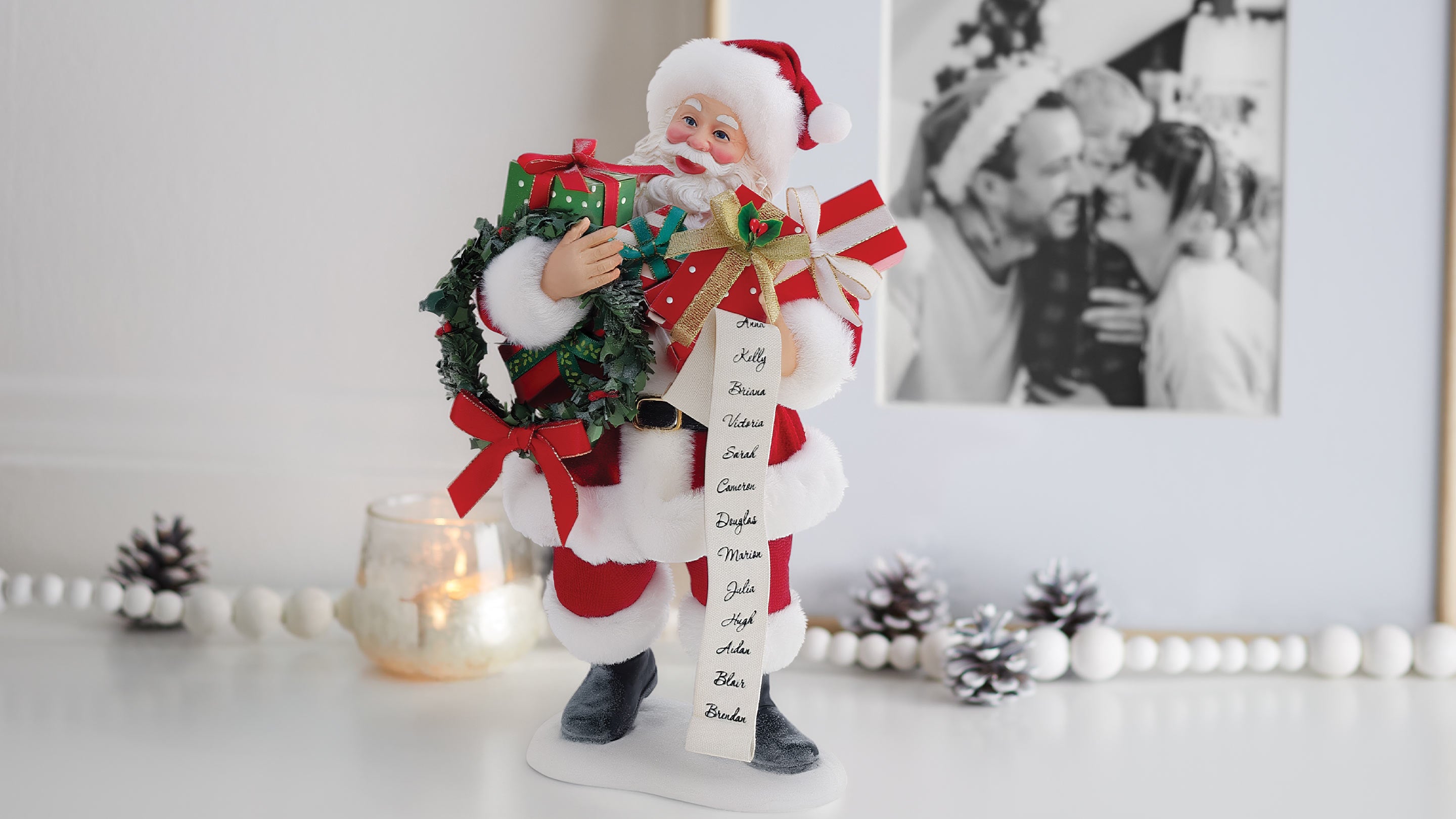 Christmas-themed figurine holding a wreath and gift with a photo in the background