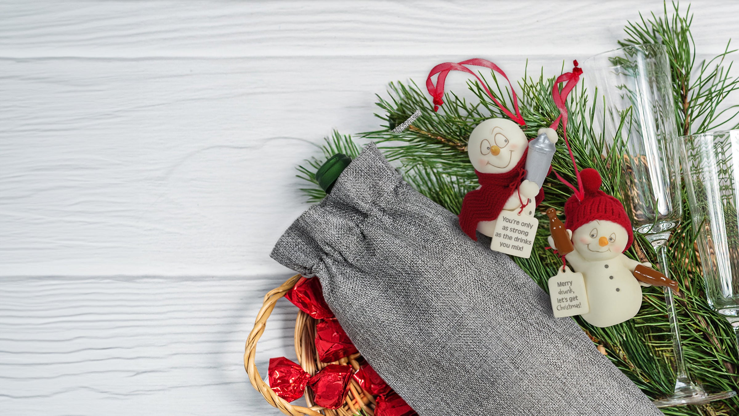 Decorative setting with Christmas ornaments, glasses, and a gray napkin on a white surface.