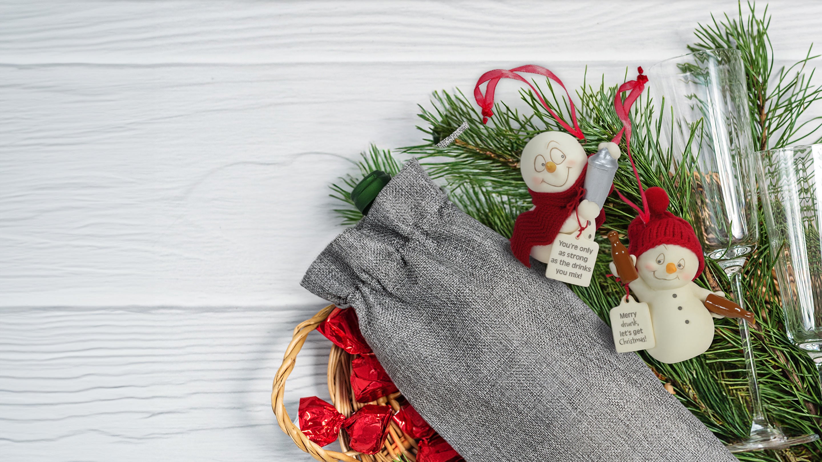 Decorative setting with Christmas ornaments, glasses, and a gray napkin on a white surface.