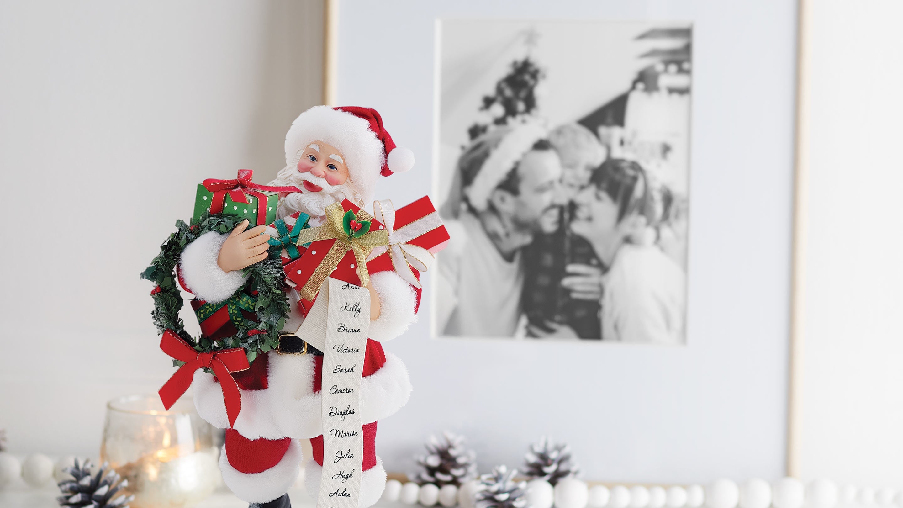 Decorative Santa Claus figure holding a wreath with a list, standing in front of a framed black and white photo.