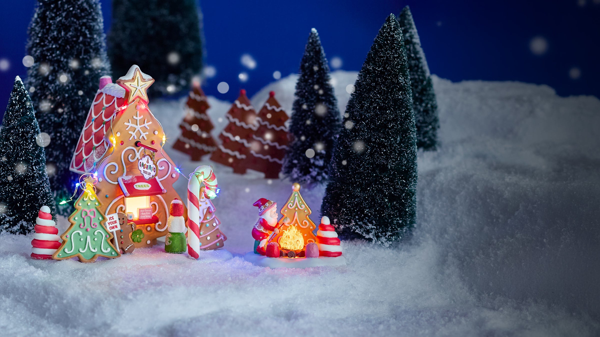 Decorative Christmas scene with lit gingerbread house, candy cane, and Santa Claus figure on a snowy background.