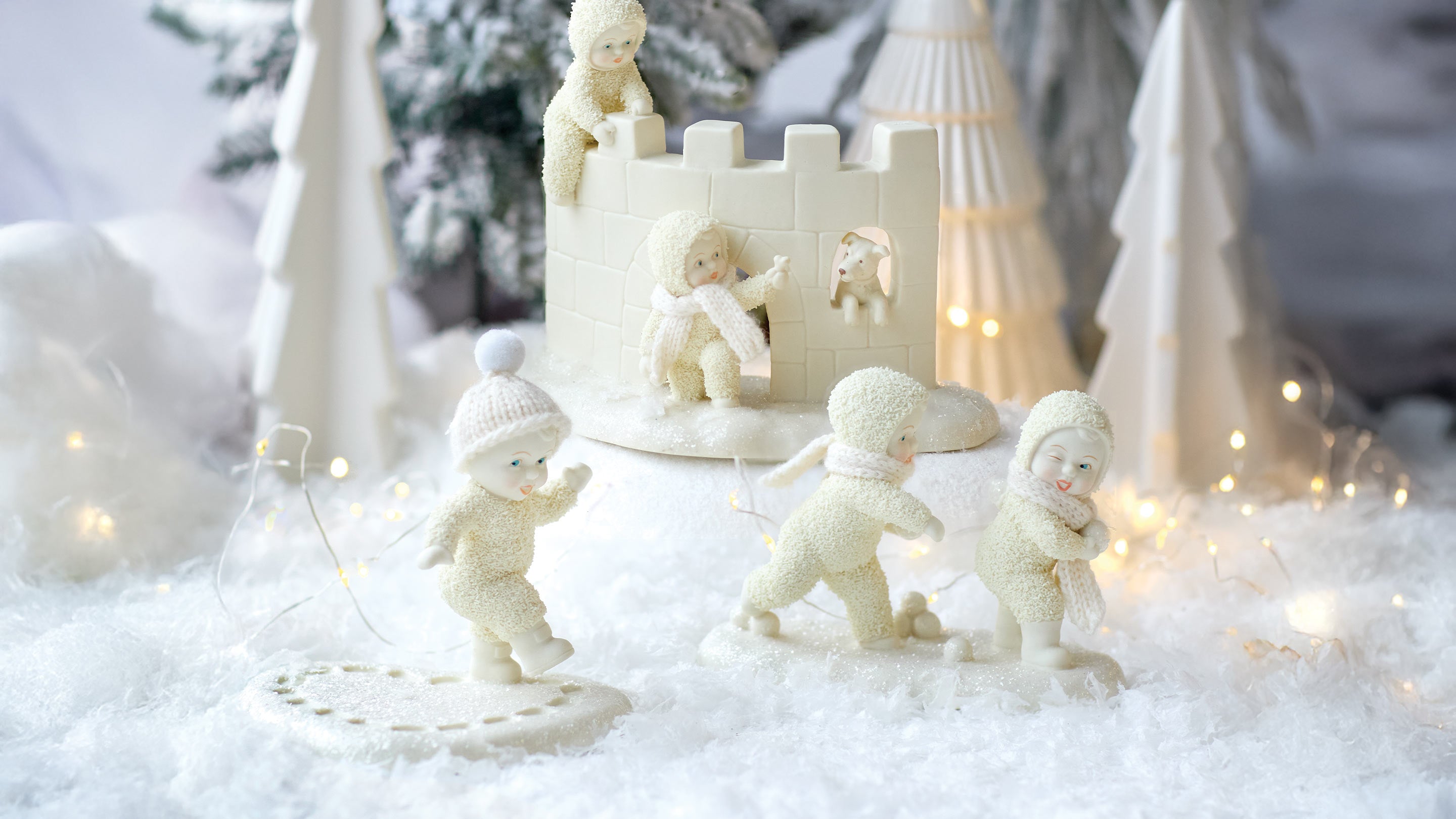 Decorative scene with white figurines of children and a castle in a snowy setting.