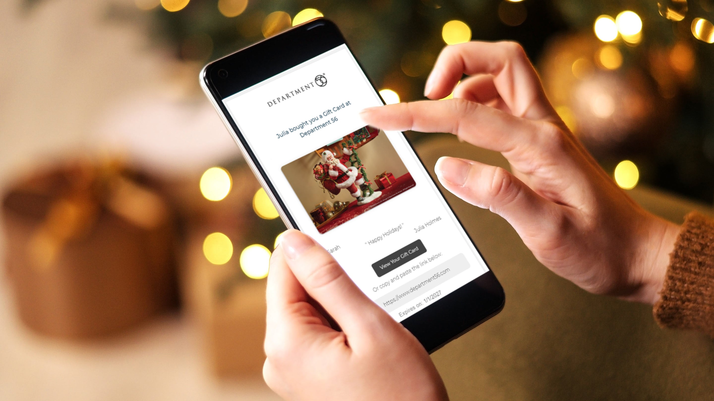 Person holding a smartphone with a Department of Defense website open, surrounded by blurred Christmas lights and presents.