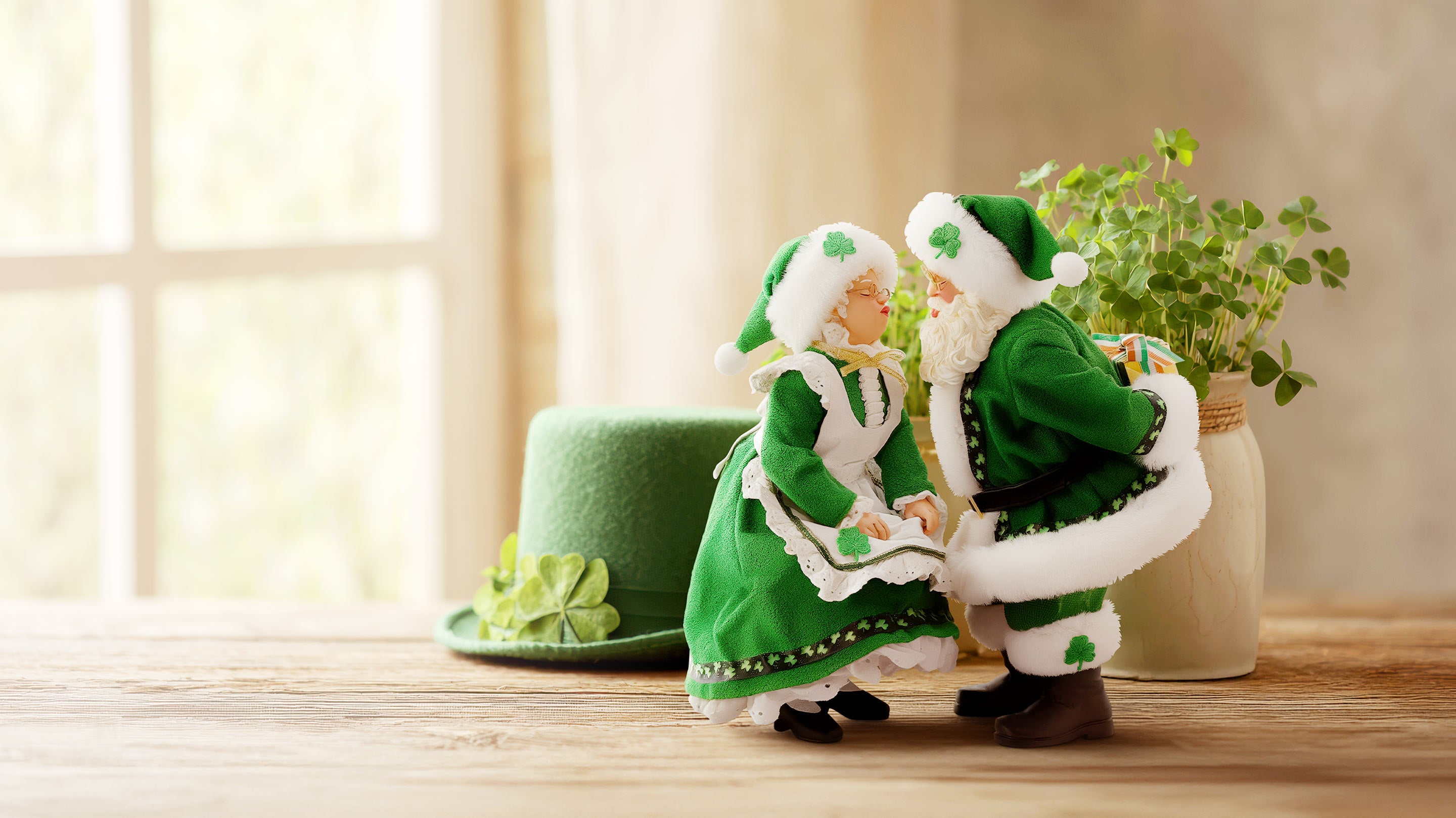 Two green and white decorative figures on a wooden surface with a plant in the background.