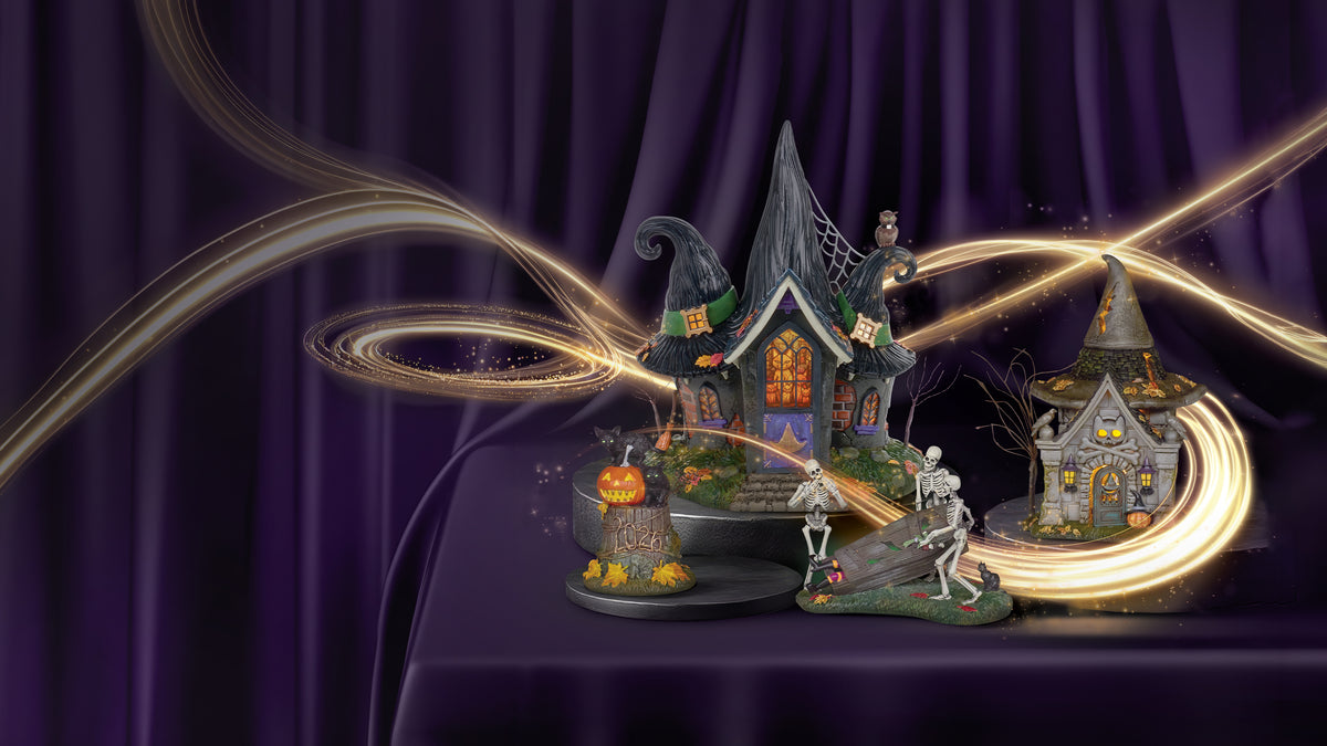 A decorative Halloween diorama set featuring two haunted houses, skeleton figures, a cauldron with a pumpkin, and swirling golden light trails against a dark purple draped background.